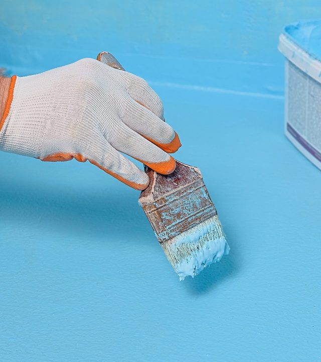 A worker is applying waterproofing paint to the floor in the bathroom.